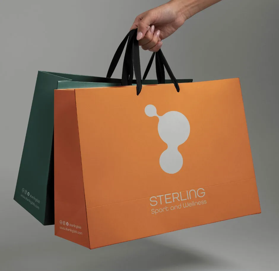 Hand holding orange and green Sterling shopping bags
